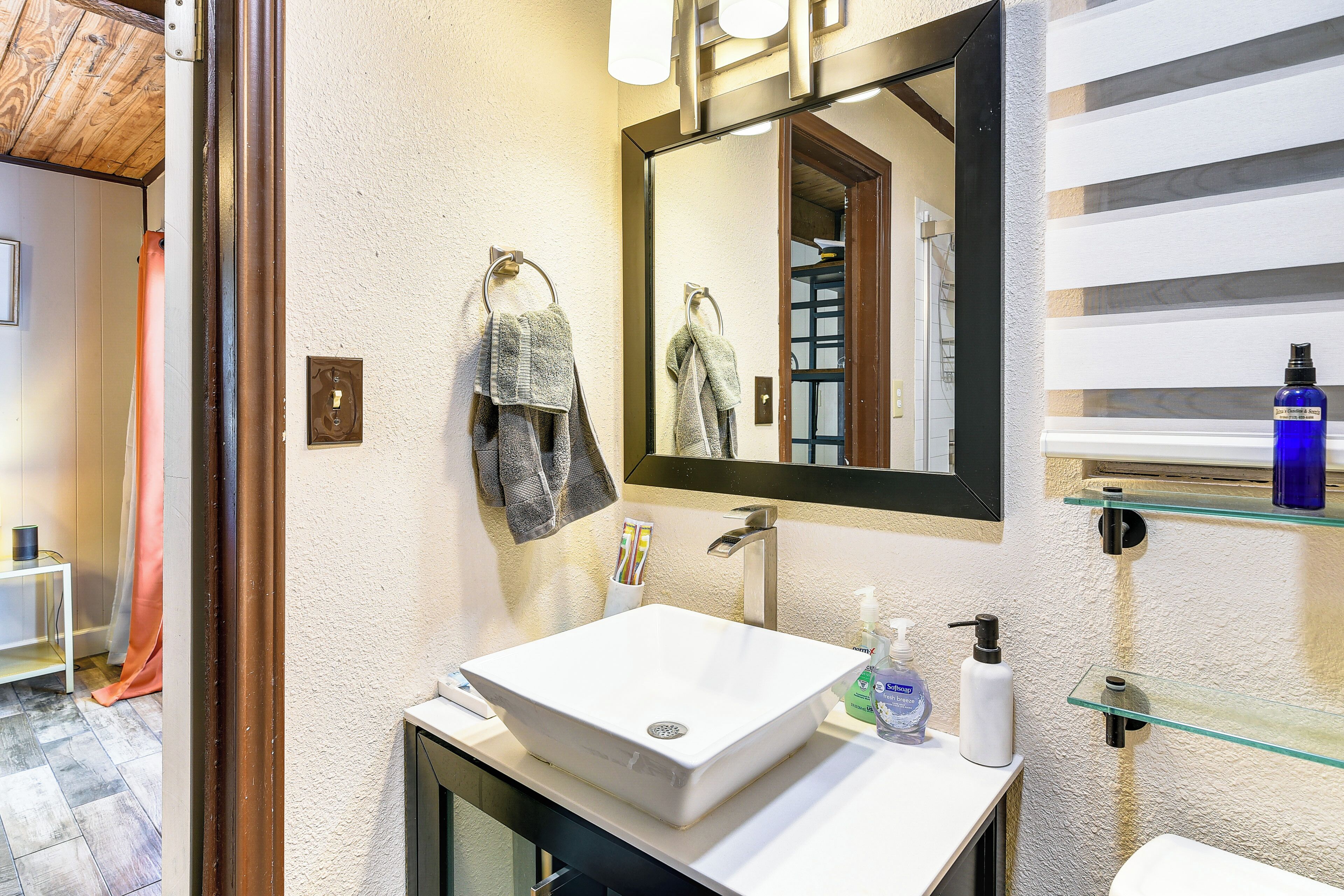 A bathroom with a white sink, a mirror, and a glass shelf with toiletries.