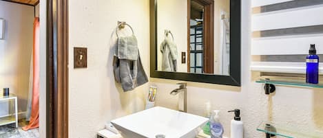 A bathroom with a white sink, a mirror, and a glass shelf with toiletries.