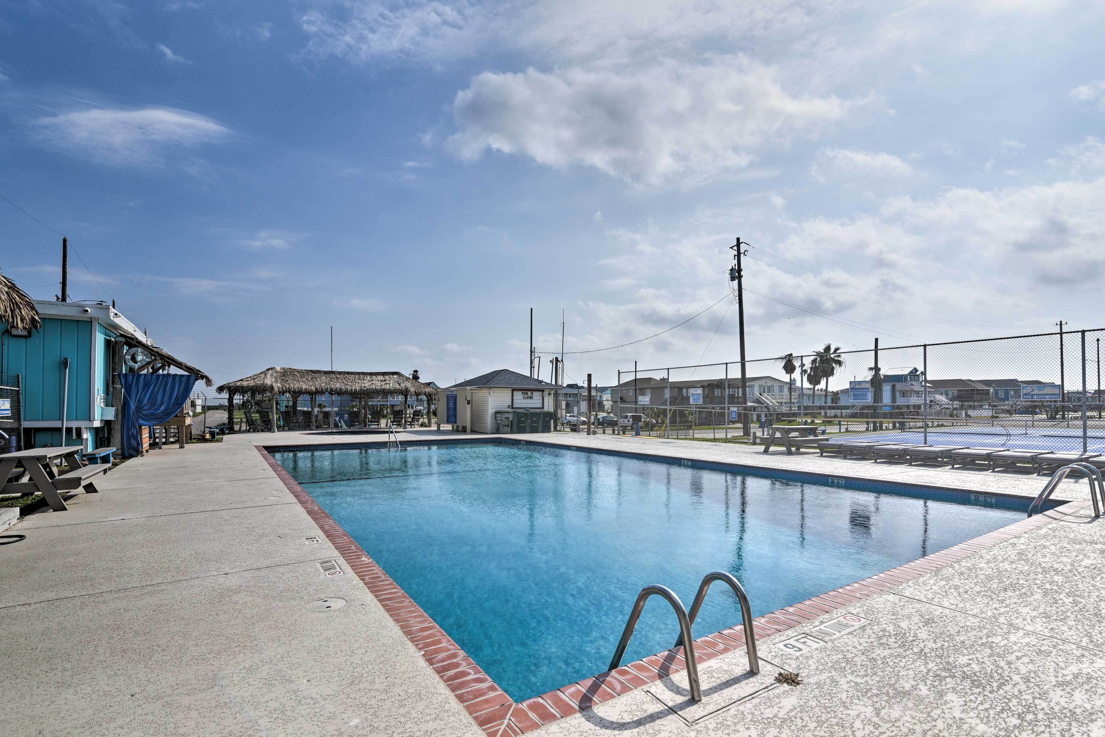 A rectangular swimming pool with a brick edge, surrounded by a fence, and a blue building to the left.