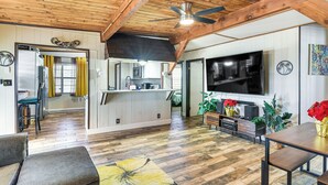 Ett rymligt vardagsrum med ett träpanelat tak, en stor TV med platt skärm och en matplats med ett träbord och stolar.