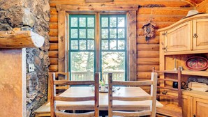 A rustic wooden cabin interior with a stone wall, a wooden dining table with chairs, a green-framed window, and wooden cabinets. - ~ 13 Mi to Main St: Park City Cabin w/ Mtn Views! (Park City)