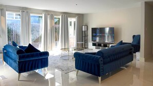 Ein modernes Wohnzimmer mit zwei blauen Sofas, einem Glastisch und einem Flachbildfernseher.