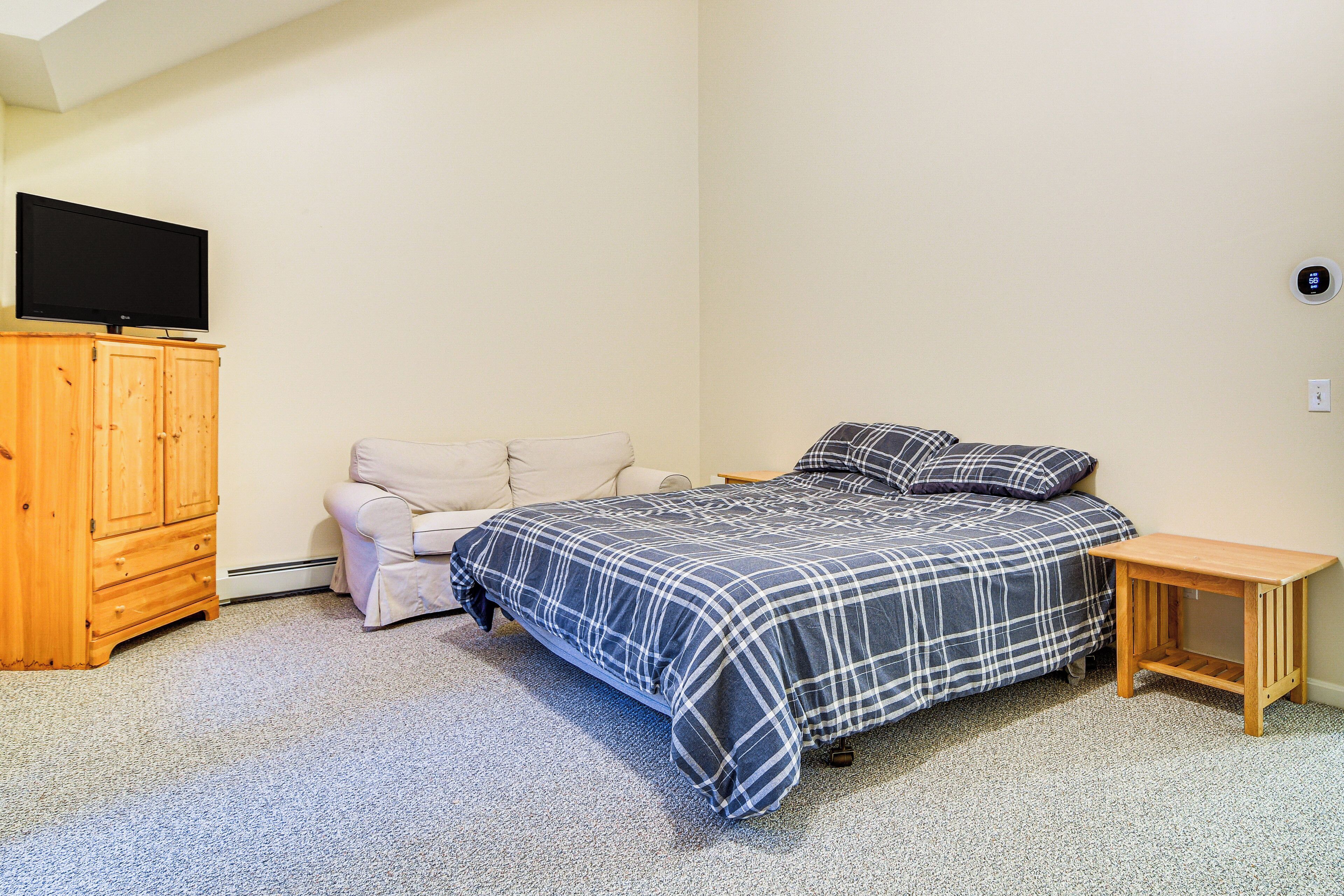 A bedroom with a bed, a wooden nightstand, a television on a cabinet, and a small table.