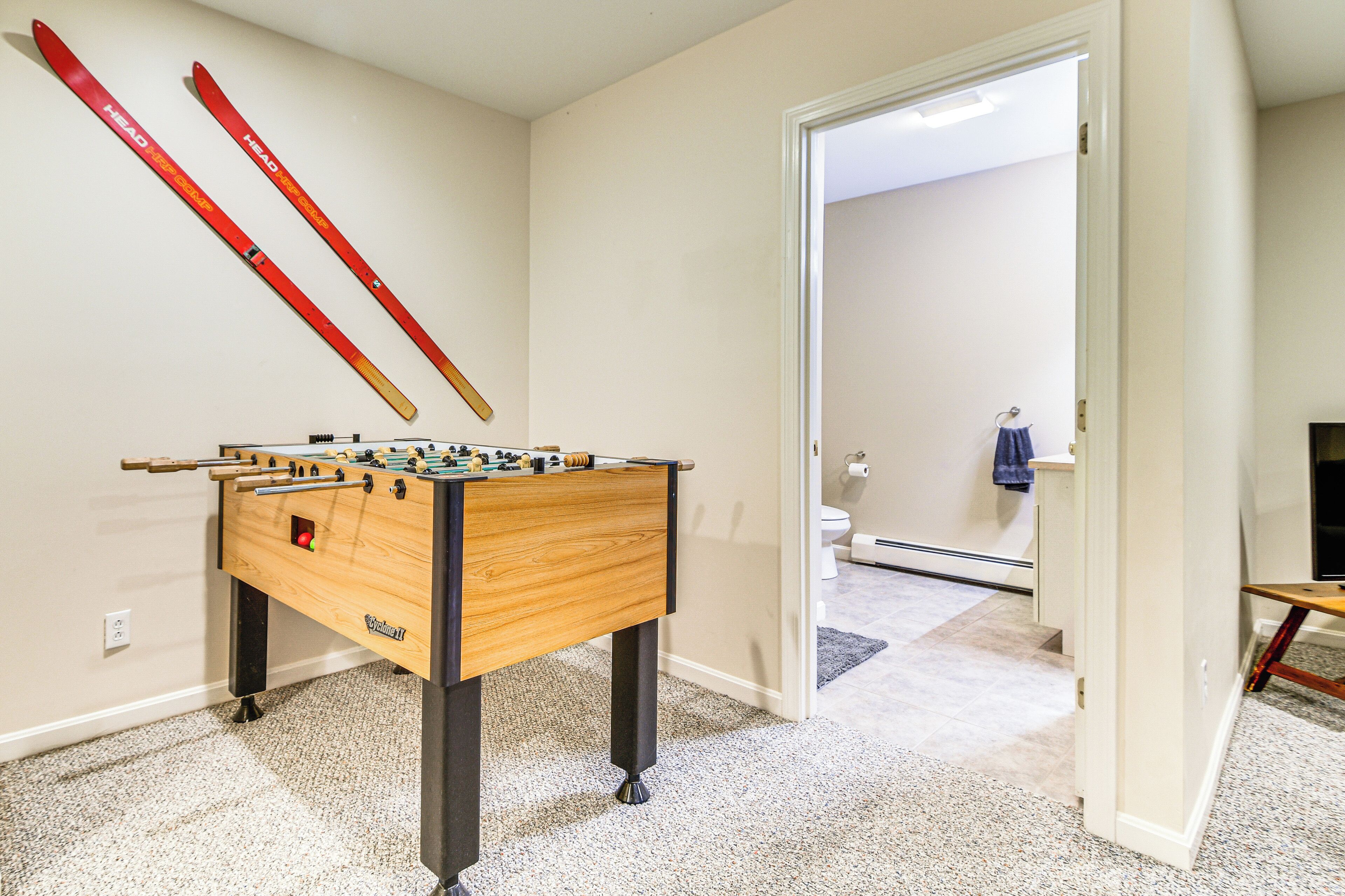Ein Zimmer mit einem Kicker, einer zur Toilette führenden Tür und einem kleinen Tisch mit einem Stuhl.