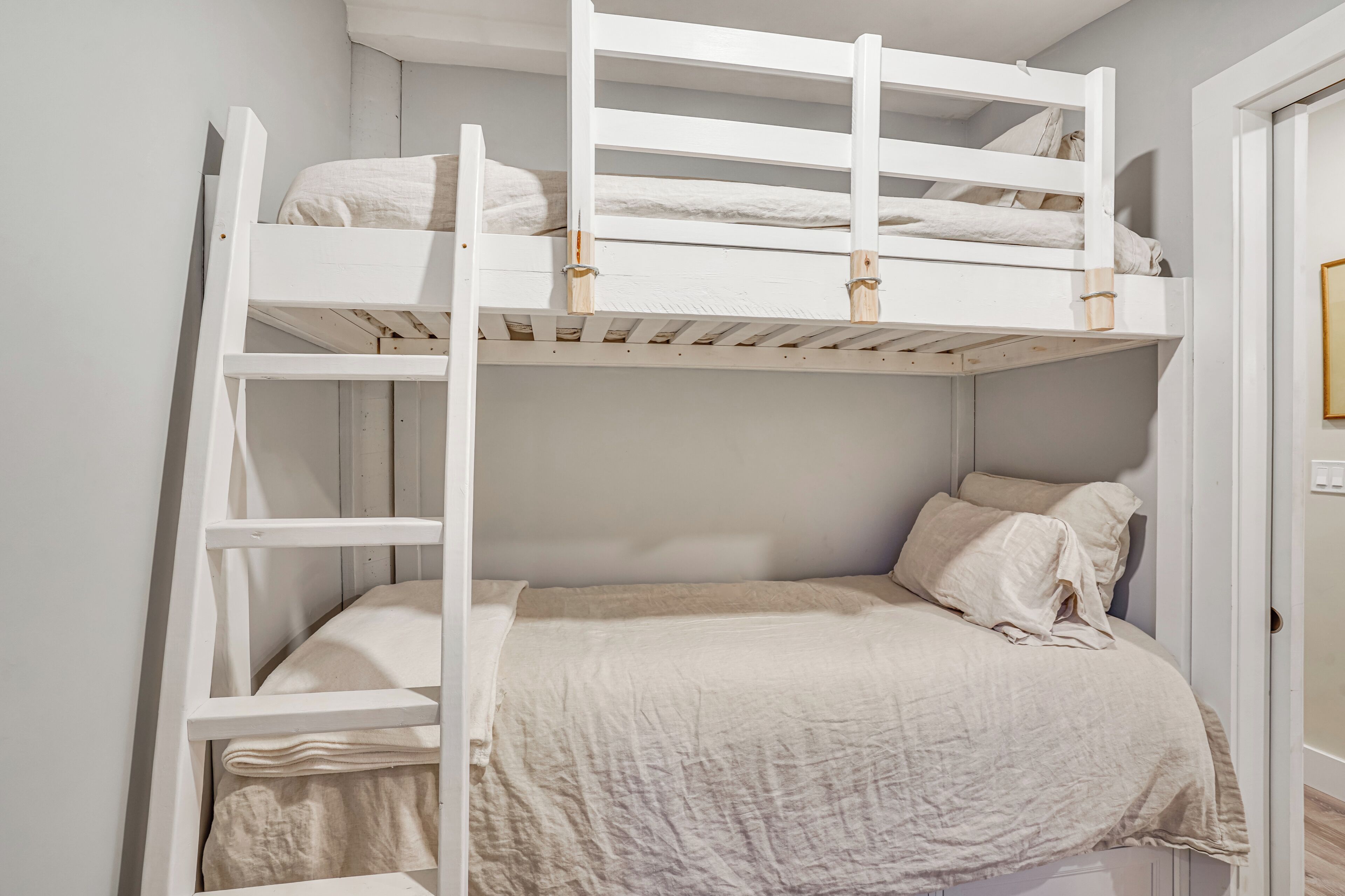 Una cama litera con escalera, una cama individual debajo y una puerta a la derecha.