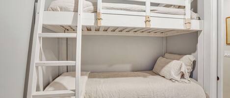 Una cama litera con escalera, una cama individual debajo y una puerta a la derecha.