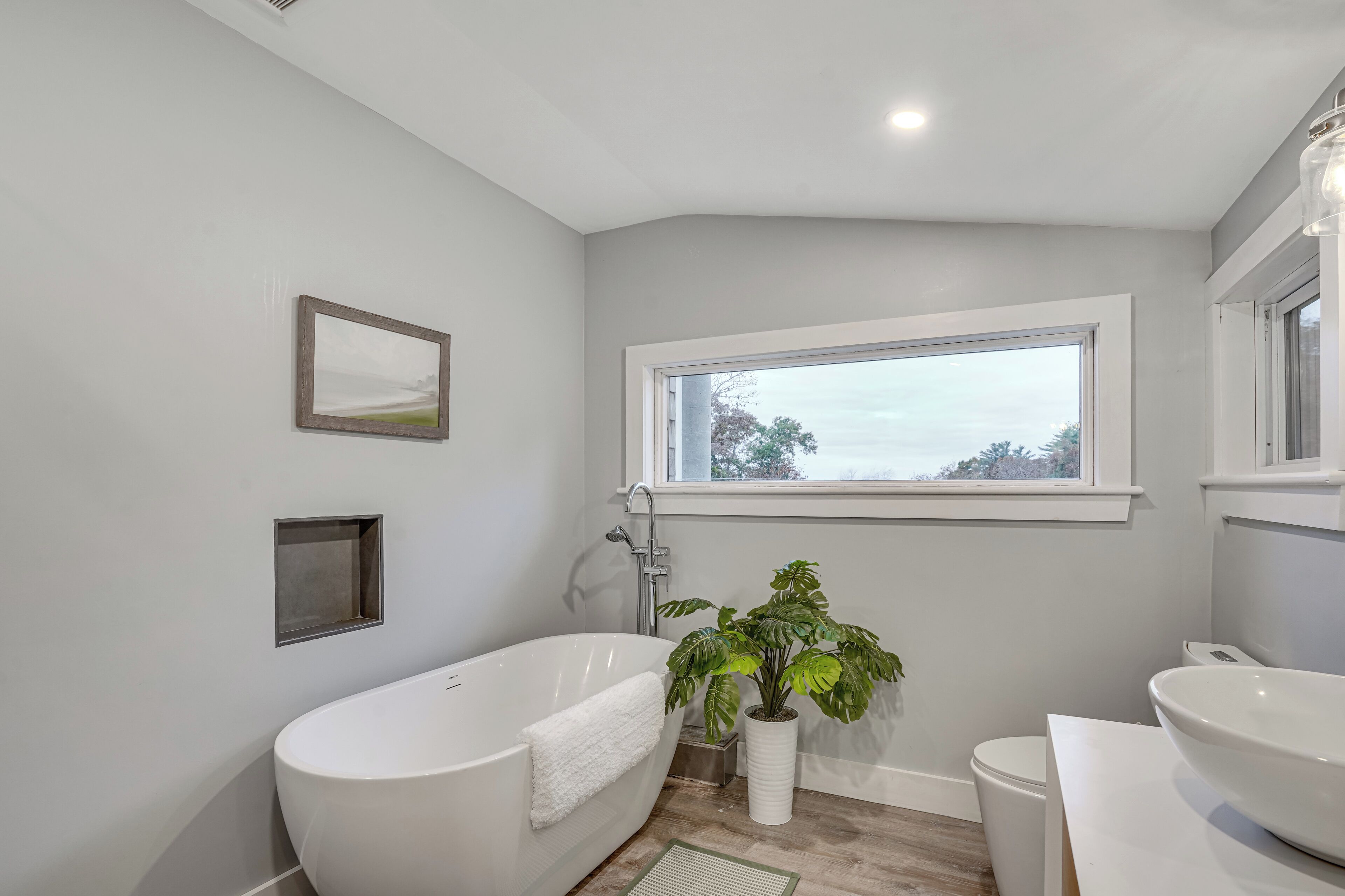 Ein modernes Badezimmer mit einer freistehenden Badewanne, einem großen Fenster und einem Blumentopf.