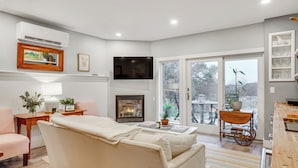 A modern living room with a fireplace, a sofa, a TV, and a dining area with a wooden table and chairs. - Airstream & Ocean View: Unique Gloucester Getaway (Gloucester)