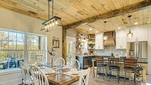 A spacious kitchen with a large island, wooden ceiling, and ample natural light from large windows.