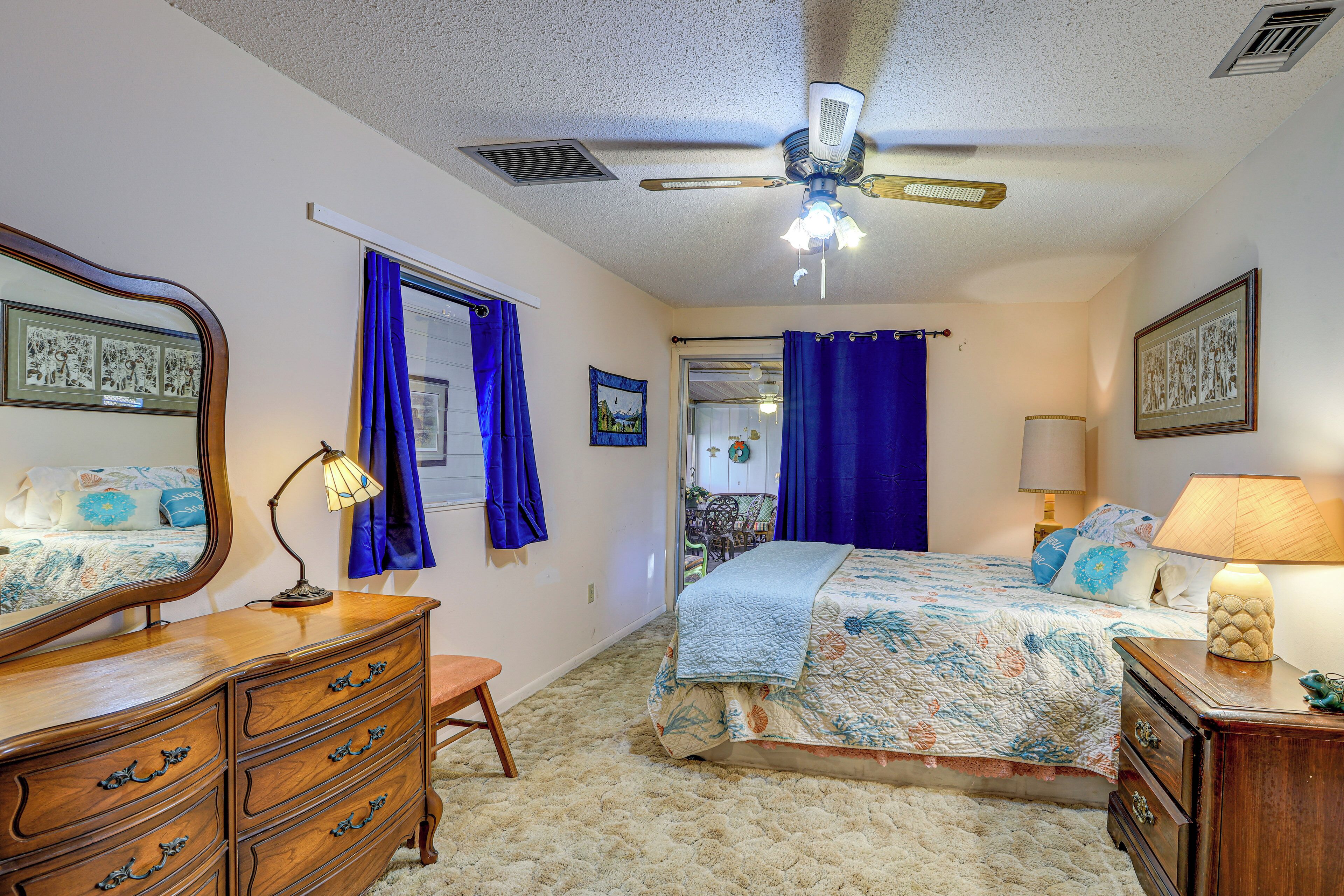 A bedroom with a bed, dresser, mirror, ceiling fan, and a view into another room.