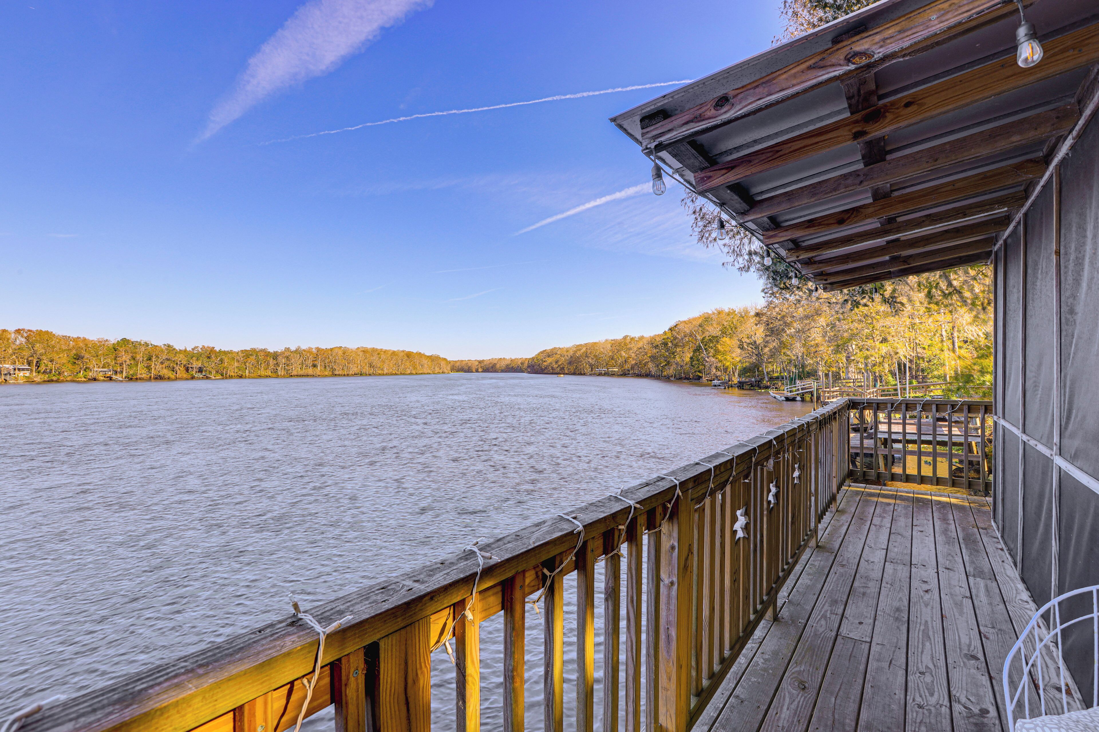A wooden deck with a railing overlooking a calm lake, surrounded by trees with autumn foliage.