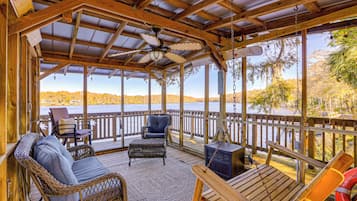 A covered deck with wicker furniture, a swing, and a view of a lake.