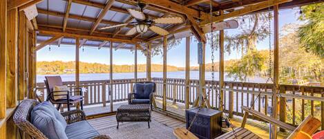 A covered deck with wicker furniture, a swing, and a view of a lake.