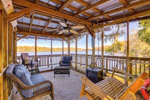 Une terrasse couverte, aménagée avec des meubles en osier, une balançoire et offrant une vue sur un lac.