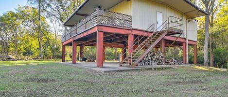 A two-story building with a balcony and a staircase leading to a covered area with a stack of firewood.