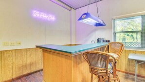 A kitchen with wooden paneling, a neon sign reading "The Poper Club", a blue hanging light fixture, and wicker chairs. - Riverfront Fishing: Home in Columbus w/ Grill (Columbus)