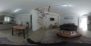 A spacious living area with a dining table, a sofa, and a spiral staircase.