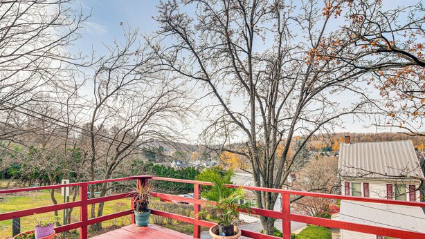 A red wooden deck with potted plants, overlooking a residential area with houses and trees.