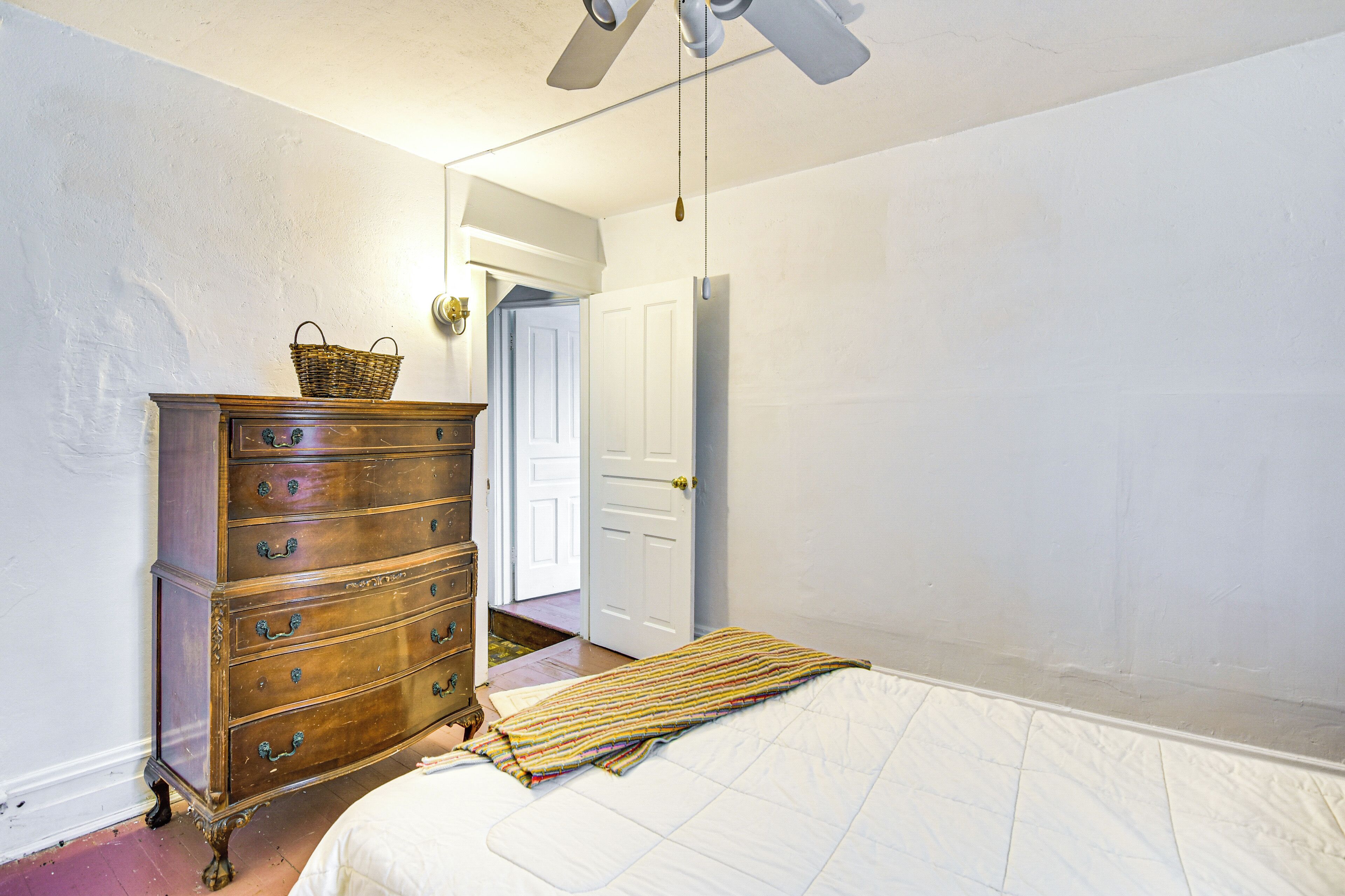 Un dormitorio con un aparador de madera, una cama, un ventilador de techo y una puerta que da a otra habitación.
