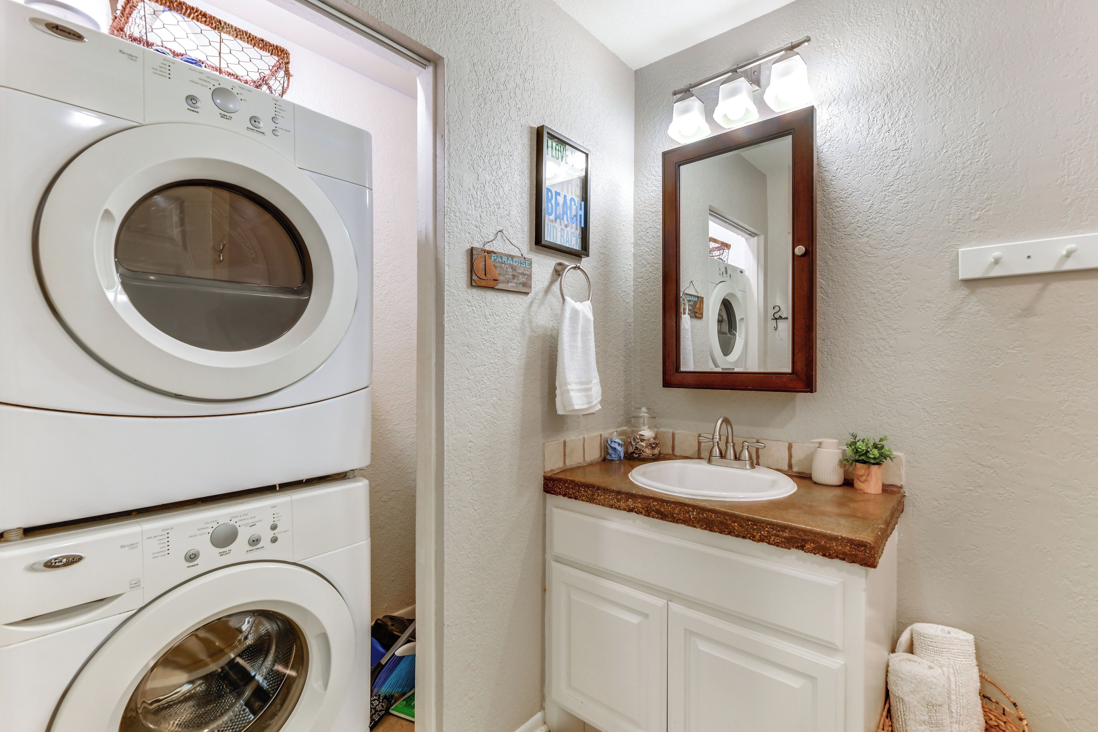 A laundry area with stacked washing machines, a sink, and a mirror.