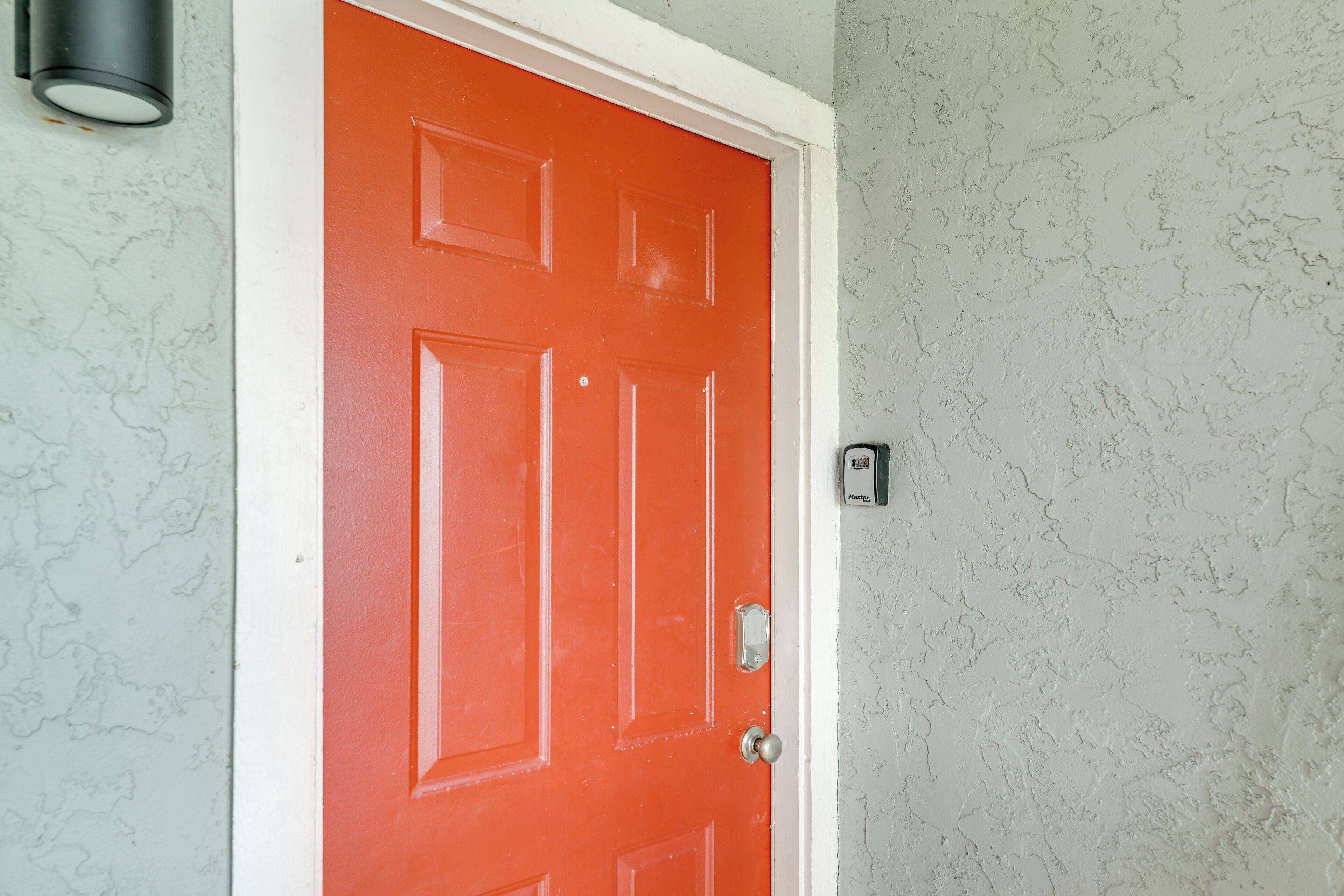 A red door with a white frame, a textured wall, and a wall-mounted light fixture.