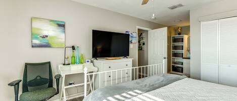 A bedroom with a bed, a desk with a chair, a television, and a ceiling fan.