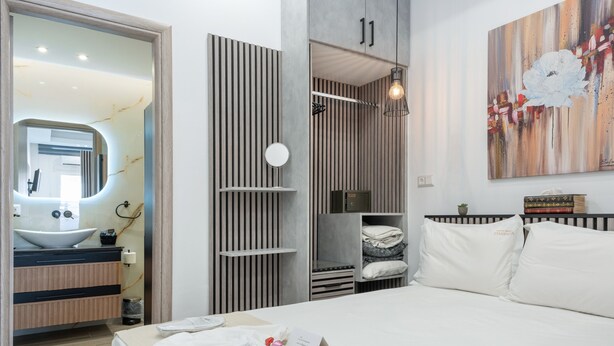 Une chambre d’hôtel moderne avec un grand lit, une salle de bain avec un lavabo et un miroir, une armoire et un tableau au mur.