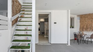 Un intérieur moderne avec un escalier, un coin repas et une cuisine visible à travers une porte ouverte.
