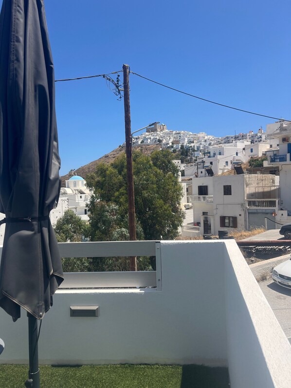 Un balcón con vistas a edificios blancos en una colina, un poste de electricidad y un objeto negro a la izquierda.
