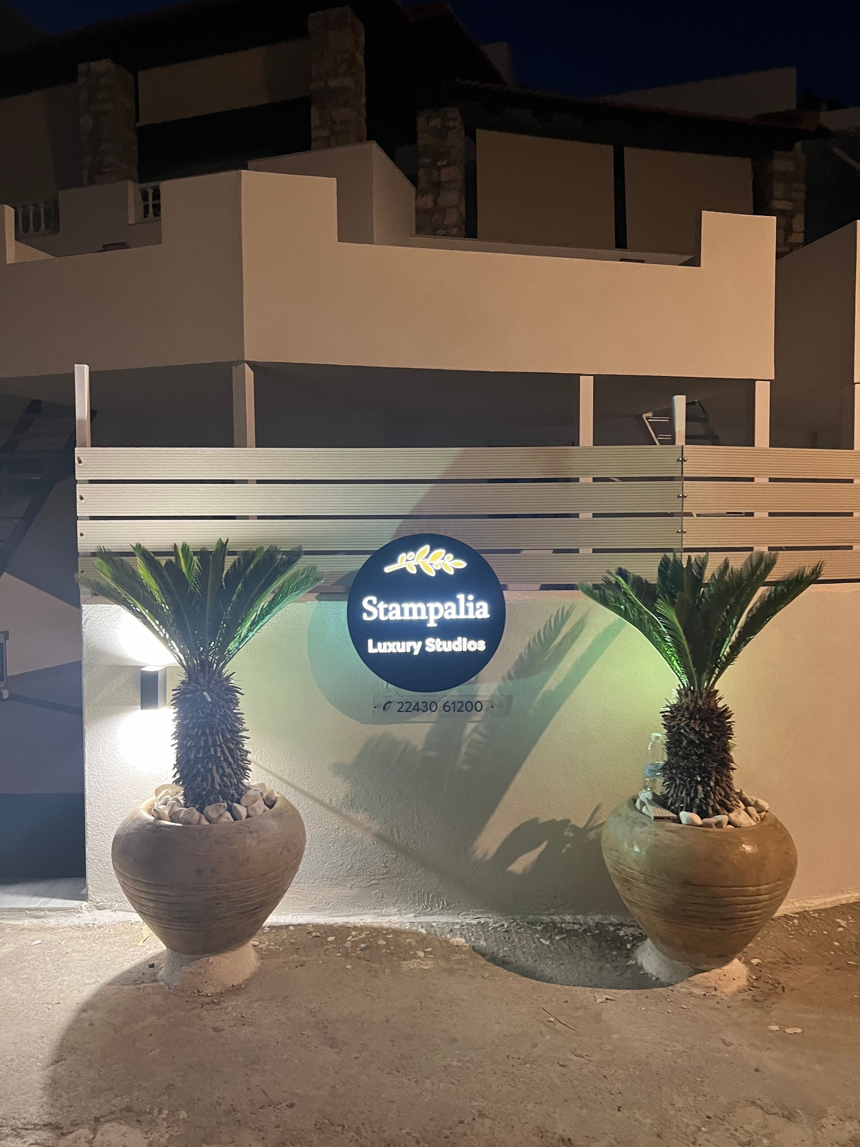 A building entrance with a sign for Stampalia Luxury Studios. There are two potted plants in front.