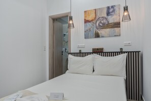 A bedroom with a bed, two pendant lights, a painting, and a bedside table.