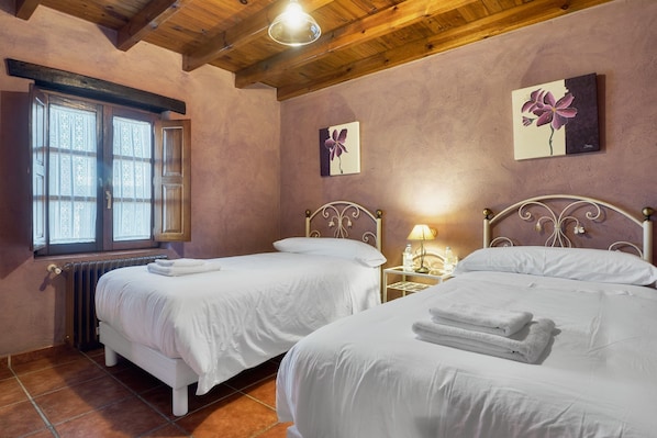 A bedroom with two beds, a radiator, a window, and artwork on the walls.