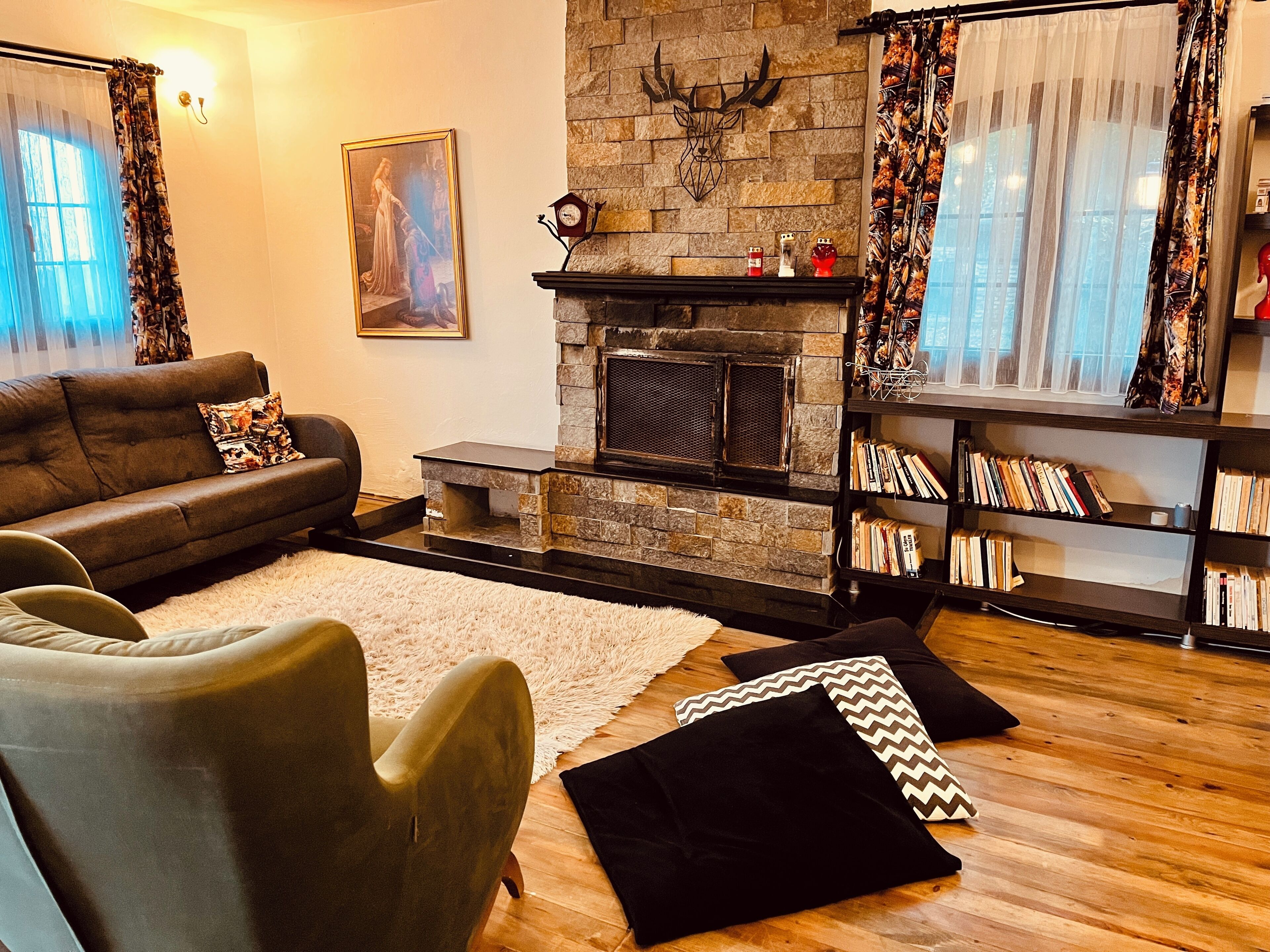 A living room with a fireplace, a sofa, a chair, a bookshelf, and a painting on the wall.