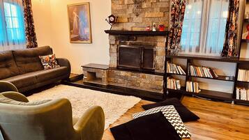 A living room with a fireplace, a sofa, a chair, a bookshelf, and a painting on the wall.