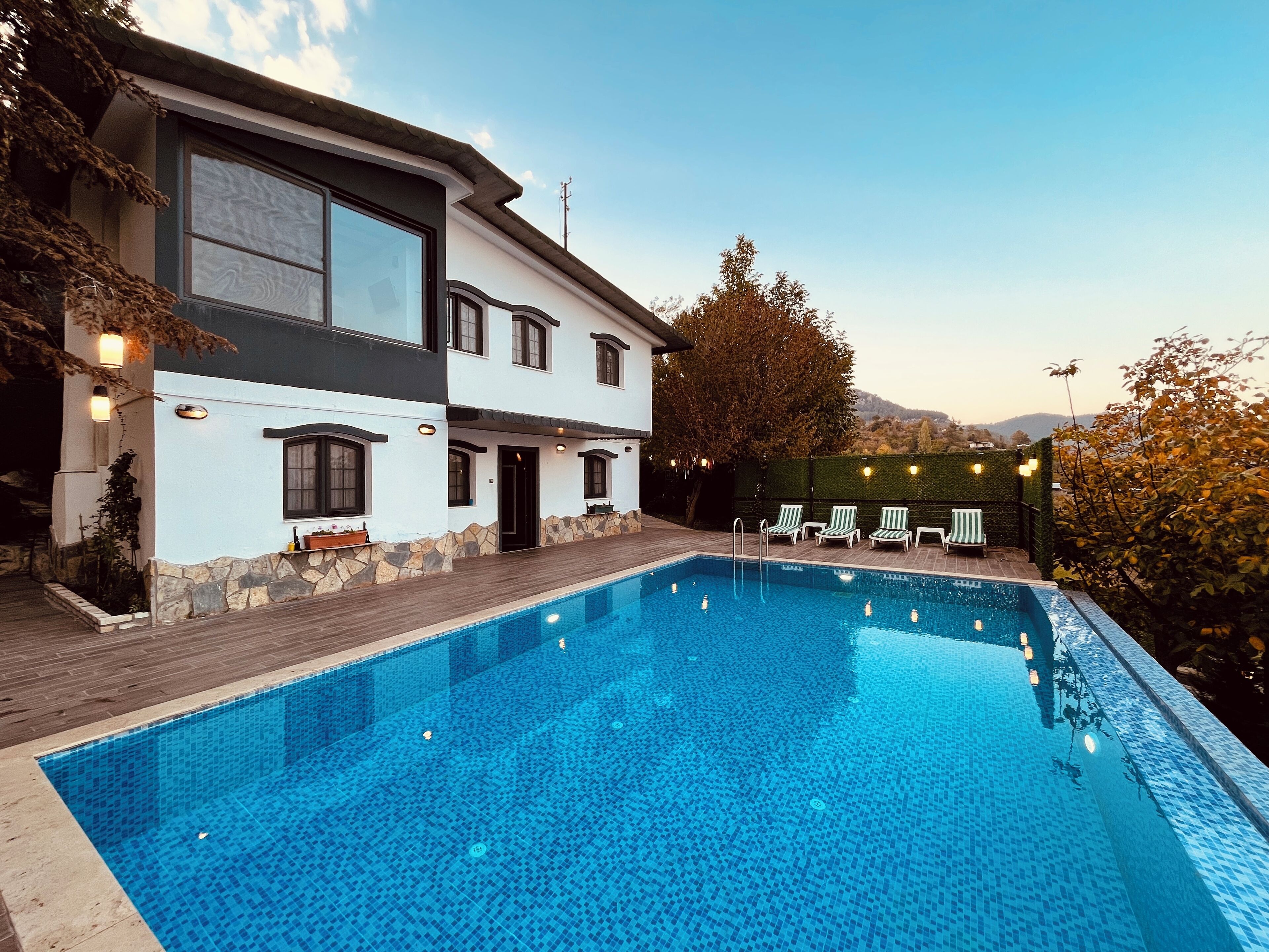 A modern two-story house with a swimming pool, stone wall, and outdoor seating area.