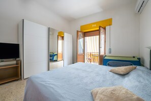 Hotellihuone, jossa on sänky, televisio, vaatekaappi ja parveke, jossa on tuoli.