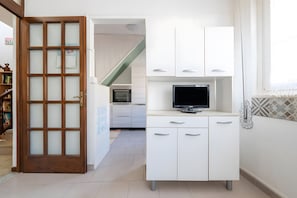 Une cuisine avec des meubles blancs, un téléviseur et une porte en bois dotée de panneaux en verre dépoli.