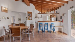 A kitchen with wooden beams, a dining area with a round table and chairs, and a bar with stools. - Holiday Home 'Casa Del Sol' with Sea View, Private Terrace and Wi-Fi (Illes Balears)
