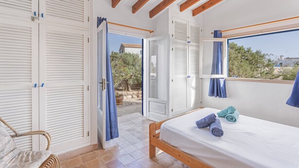 A bedroom with a bed, a chair, a wardrobe, and a window with curtains. - Holiday Home 'Casa Del Sol' with Sea View, Private Terrace and Wi-Fi (Illes Balears)