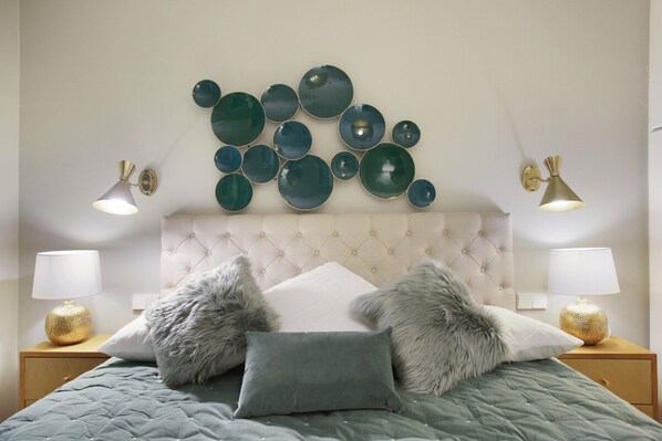 Une chambre à coucher avec une tête de lit capitonnée, une couvre-lit matelassée verte, deux oreillers moelleux et une décoration murale en forme d’assiette.