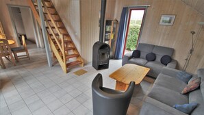 A living room with a sofa, a wooden table, a black chair, a staircase, and a fireplace. - Ferienhaus im Ferienpark Mirow (Mirow)