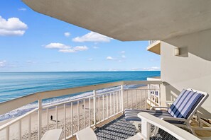 A balcony with a view of the ocean, a lounge chair, and a patterned floor.