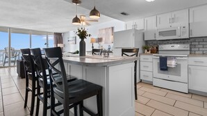 Una cocina moderna con armarios blancos, una isla central con taburetes de bar, microondas, horno e iluminación colgante.