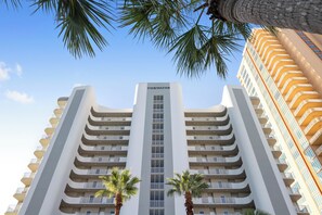 A high-rise hotel with a central vertical sign reading "TIDEWATER," multiple balconies, and palm trees in front.