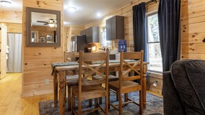 Ein Holzinterieur mit Esstisch und Stühlen, Deckenventilator und einem Fenster mit Vorhängen.