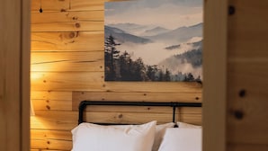 Ein Schlafzimmer in einer Holzhütte mit einem Bett, einem Deckenventilator und einem Gemälde einer Berglandschaft an der Wand.
