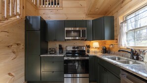 Una cucina moderna con mobili verde scuro, elettrodomestici in acciaio inossidabile e soffitto in legno.