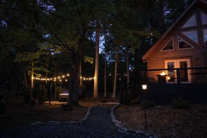 A wooden cabin with a porch, surrounded by trees and a gravel path.