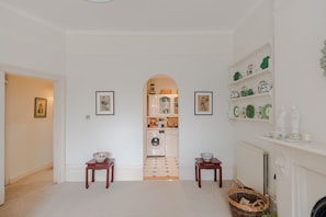 Enter a spacious hallway leading to a modern kitchen with white cabinetry and a tiled backsplash.