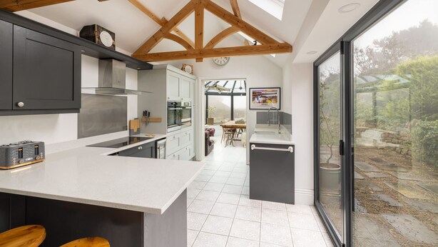 A modern kitchen with a large island, wooden beams, and a view of the garden through large windows. - Host Stay Ranworth (Scarborough)
